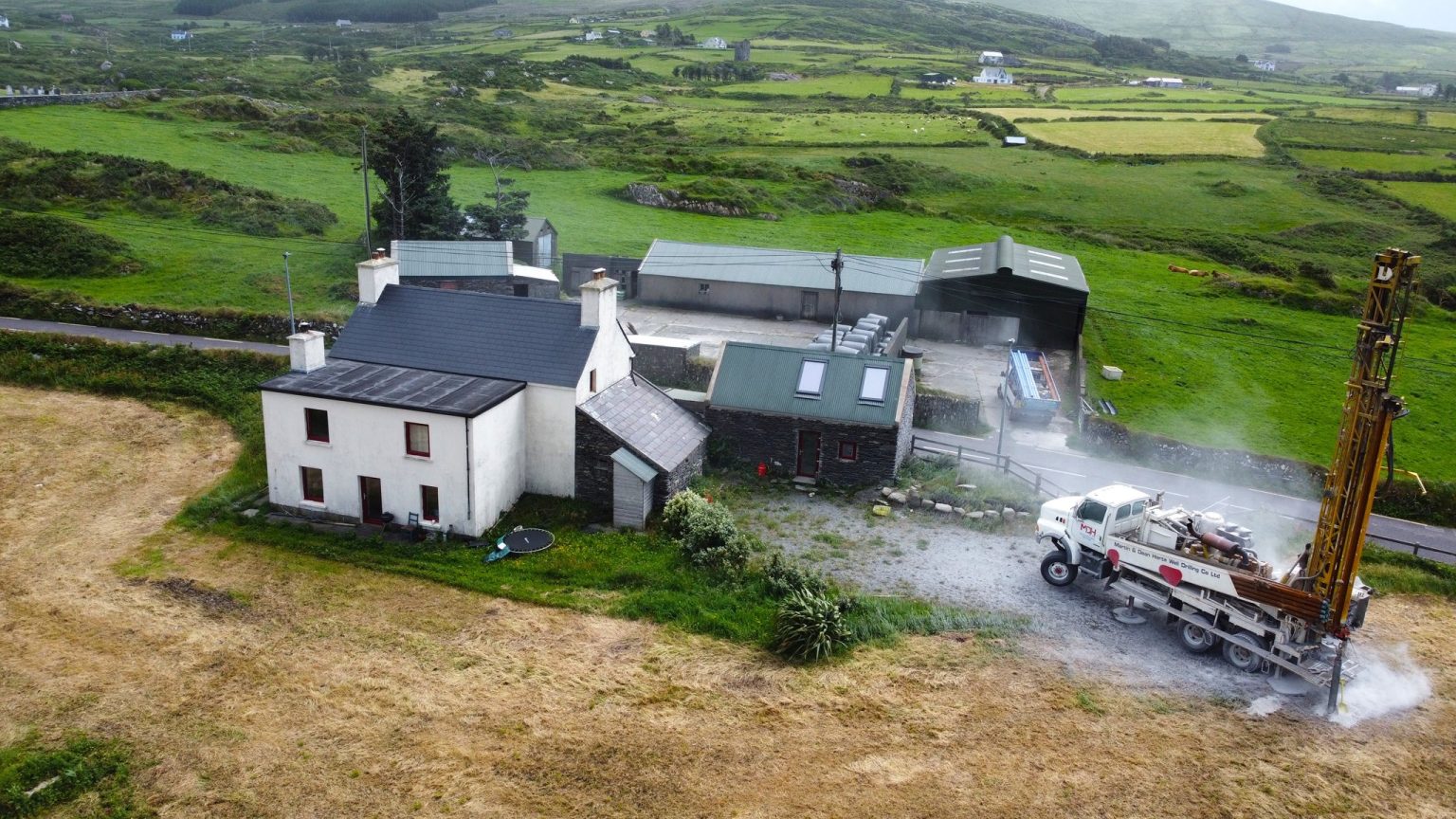 Aerial view of a well drilling rig at work beside a traditional farmhouse in the Irish countryside